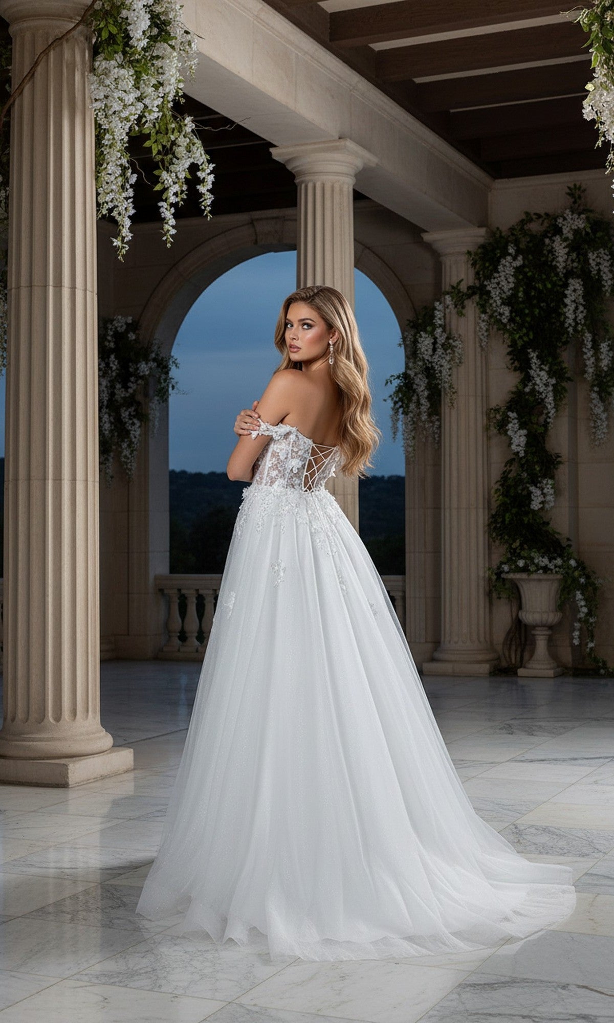A woman wearing the Cinderella Couture 8403J long prom dress in white, featuring off-the-shoulder lace details, stands on a marble floor and looks over her shoulder in an elegant setting with columns.